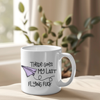 White mug with humorous text and paper airplane design on a surface with a plant in the background